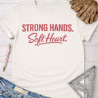 Women's funny woodworking graphic tee shirt for female woodworkers, makers, and DIY builders — Sawdust & Ponytails. White cotton t-shirt with "Strong Hands. Soft Heart." in red script.