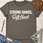 Women's funny woodworking graphic tee shirt for female woodworkers, makers, and DIY builders — Sawdust & Ponytails. Dark gray t-shirt with "Strong Hands. Soft Heart." in white text.