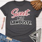 Women's funny woodworking graphic tee shirt for female woodworkers, makers, and DIY builders — Sawdust & Ponytails. Dark gray tee with "Sweet But Sawdusty" in pink and white text.