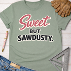 Women's funny woodworking graphic tee shirt for female woodworkers, makers, and DIY builders — Sawdust & Ponytails. Sage green t-shirt with "Sweet But Sawdusty" in pink and black.