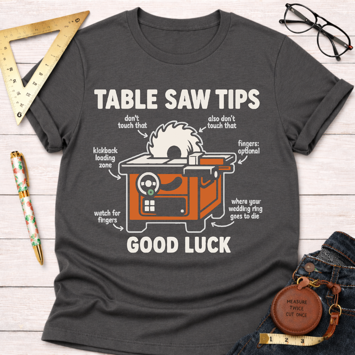 Women's funny woodworking graphic tee shirt for female woodworkers, makers, and DIY builders — Sawdust & Ponytails. Dark gray crew neck t-shirt with a humorous "Table Saw Tips Good Luck" graphic.