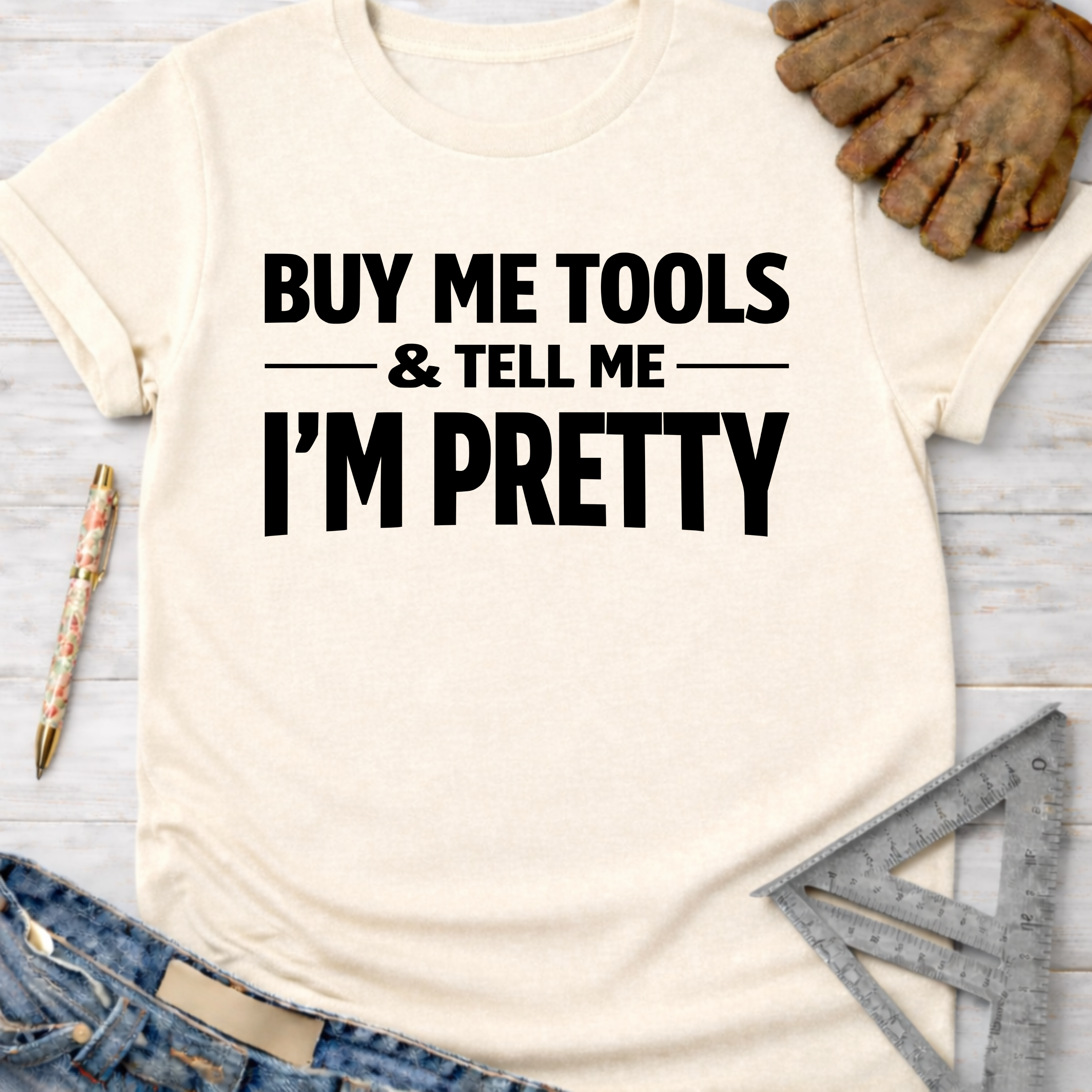 Women's funny woodworking graphic tee shirt for female woodworkers, makers, and DIY builders — Sawdust & Ponytails. Cream t-shirt with "BUY ME TOOLS & TELL ME I'M PRETTY" in black text, styled with jeans, work gloves, and tools.