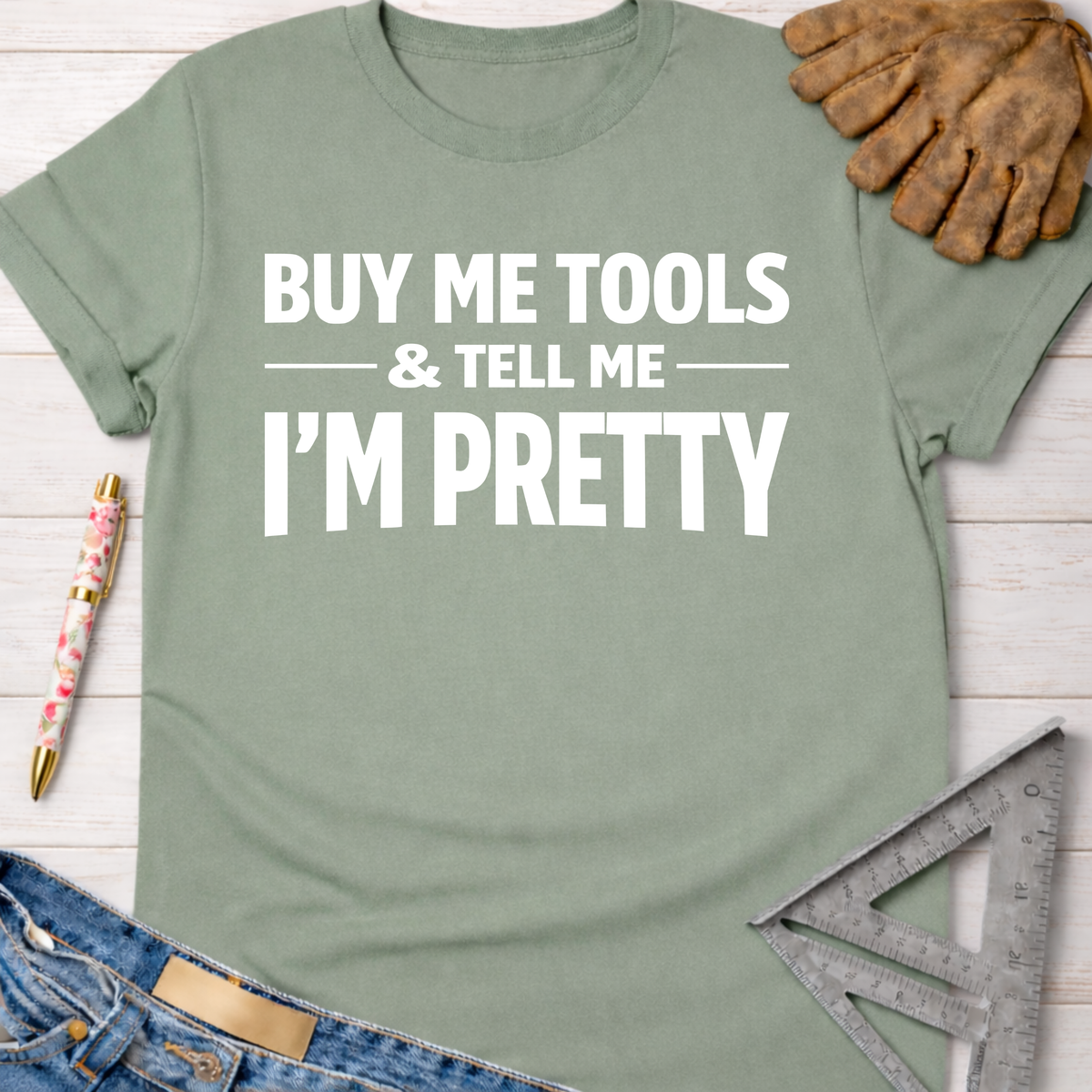 Women's funny woodworking graphic tee shirt for female woodworkers, makers, and DIY builders — Sawdust & Ponytails. Sage green cotton tee with "BUY ME TOOLS & TELL ME I'M PRETTY" in white text.