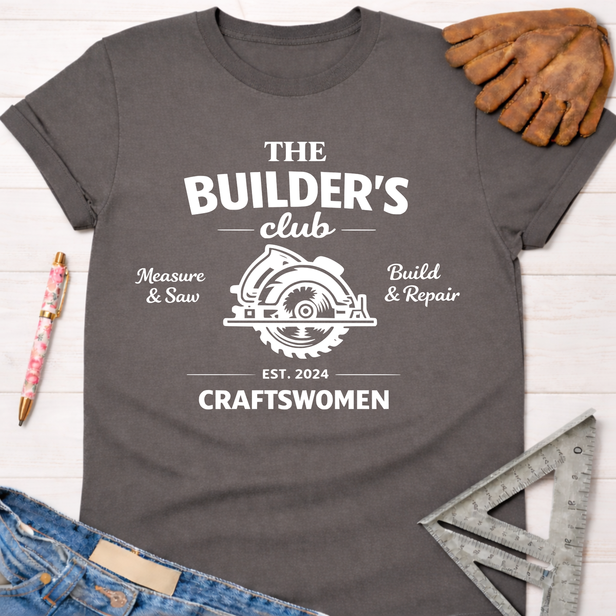 Women's funny woodworking graphic tee shirt for female woodworkers, makers, and DIY builders — Sawdust & Ponytails. Dark gray cotton tee with "The Builder's Club" circular saw graphic.