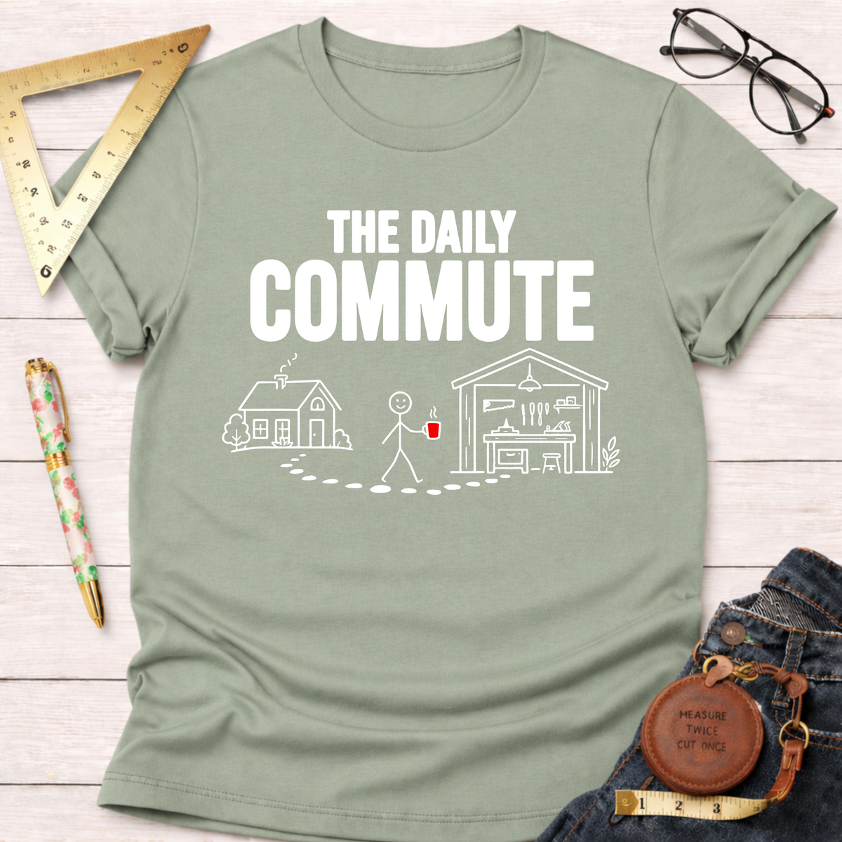 Light green cotton t-shirt with "THE DAILY COMMUTE" graphic showing a stick figure walking from a house to a workshop.
