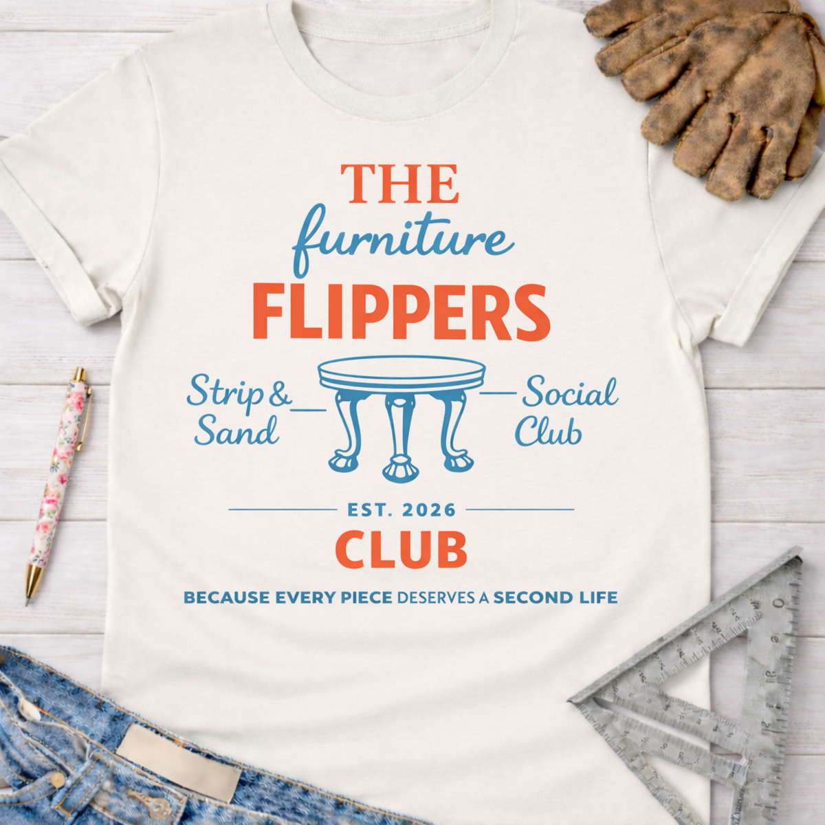Women's funny woodworking graphic tee shirt for female woodworkers, makers, and DIY builders — Sawdust & Ponytails. Cream t-shirt with "The Furniture Flippers Social Club" logo, blue and orange text, and a small table graphic.