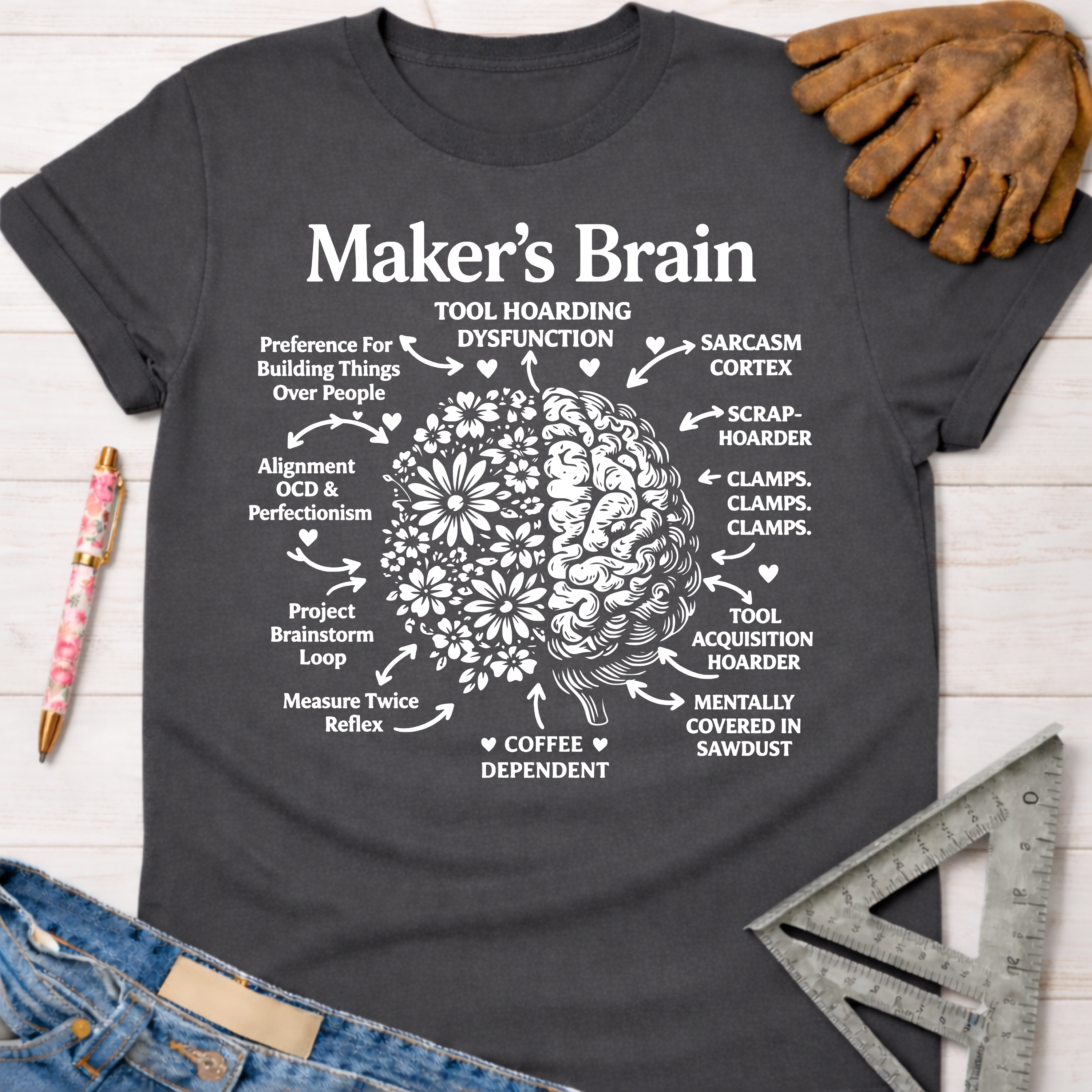 Women's funny woodworking graphic tee shirt for female woodworkers, makers, and DIY builders — Sawdust & Ponytails. Dark gray t-shirt with a white "Maker's Brain" graphic showing a brain split between flowers and gears, labeled with humorous maker traits.