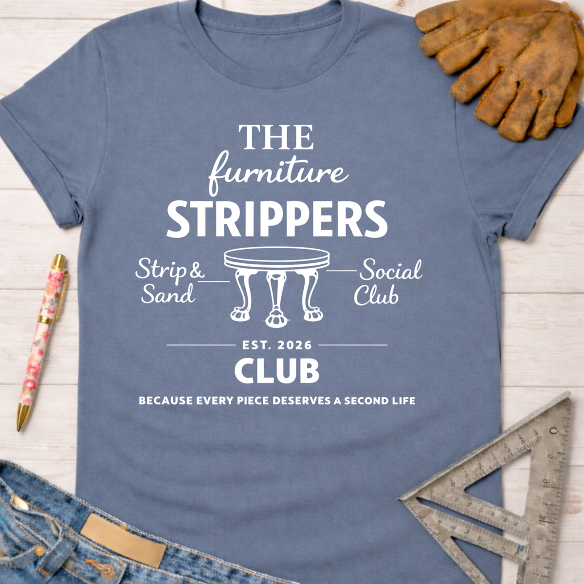 Women's funny woodworking graphic tee shirt for female woodworkers, makers, and DIY builders — Sawdust & Ponytails. Light blue cotton tee with white "The Furniture Strippers Social Club" graphic, a table icon, and "Strip & Sand" text.