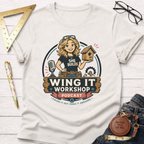 Women's funny woodworking graphic tee shirt for female woodworkers, makers, and DIY builders — Sawdust & Ponytails. Cream short-sleeve tee with "Wing It Workshop" graphic featuring a blonde woman holding a birdhouse.