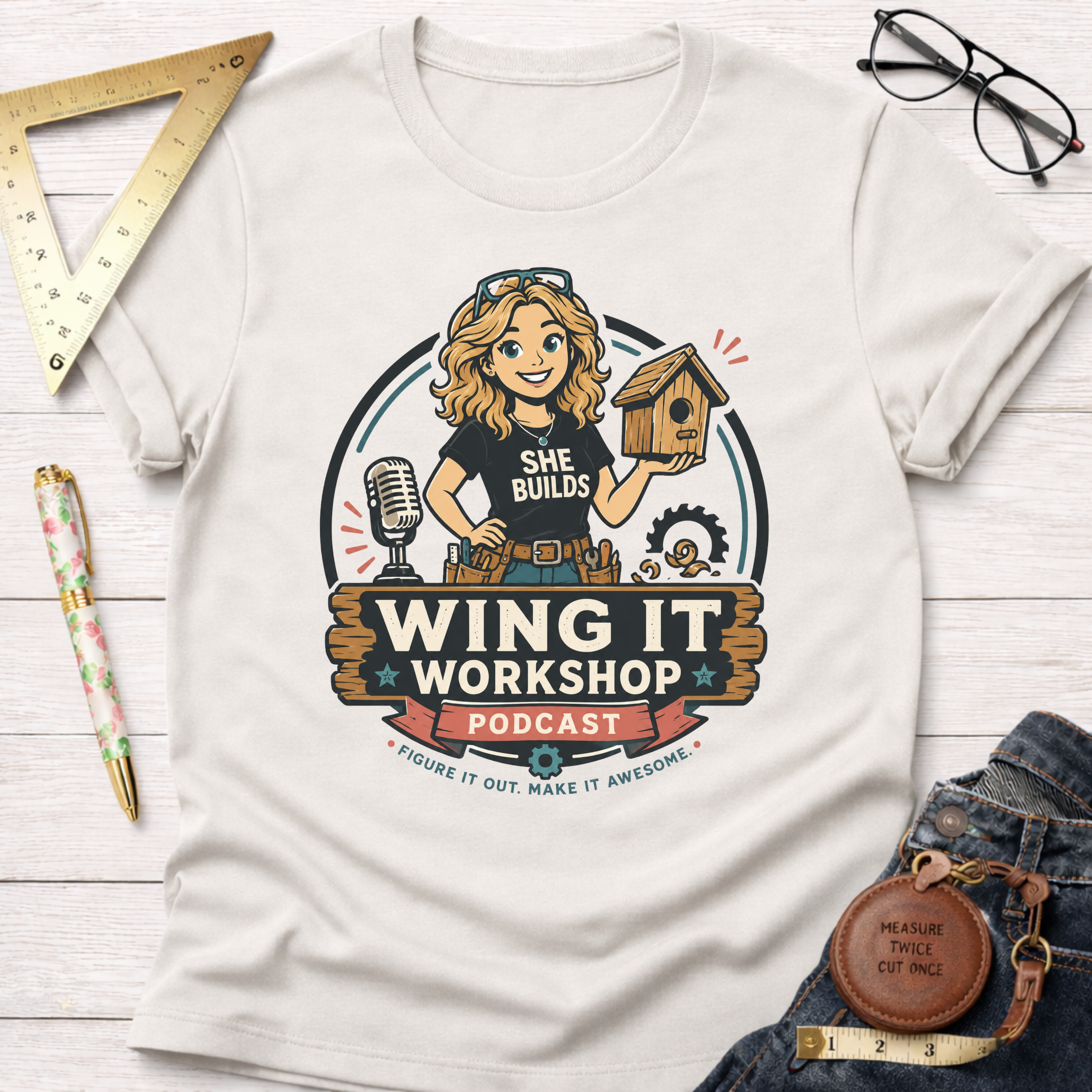 Women's funny woodworking graphic tee shirt for female woodworkers, makers, and DIY builders — Sawdust & Ponytails. Cream short-sleeve tee with "Wing It Workshop" graphic featuring a blonde woman holding a birdhouse.
