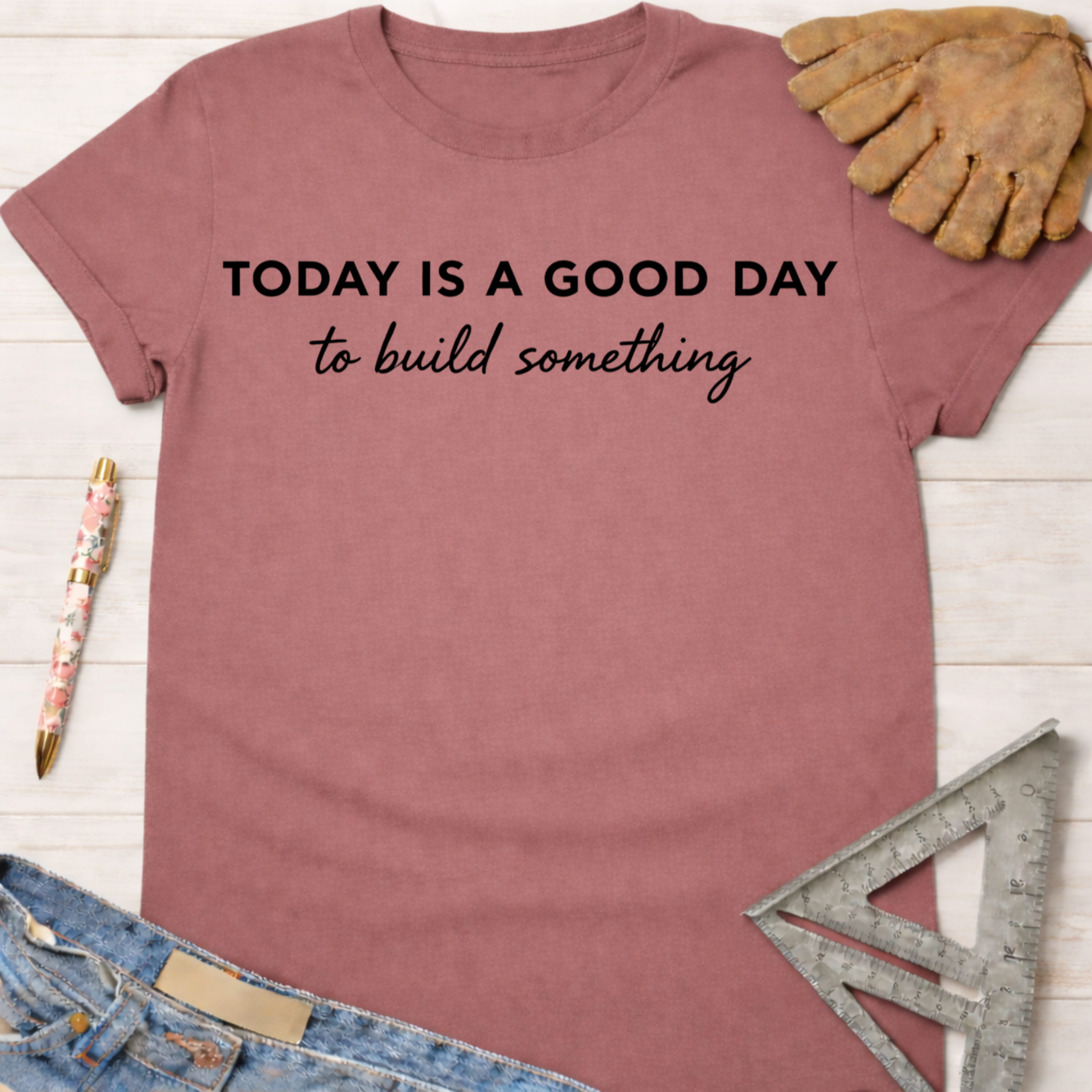 Women's funny woodworking graphic tee shirt for female woodworkers, makers, and DIY builders — Sawdust & Ponytails. Mauve cotton t-shirt with "TODAY IS A GOOD DAY to build something" in black text, next to a work glove and ruler.