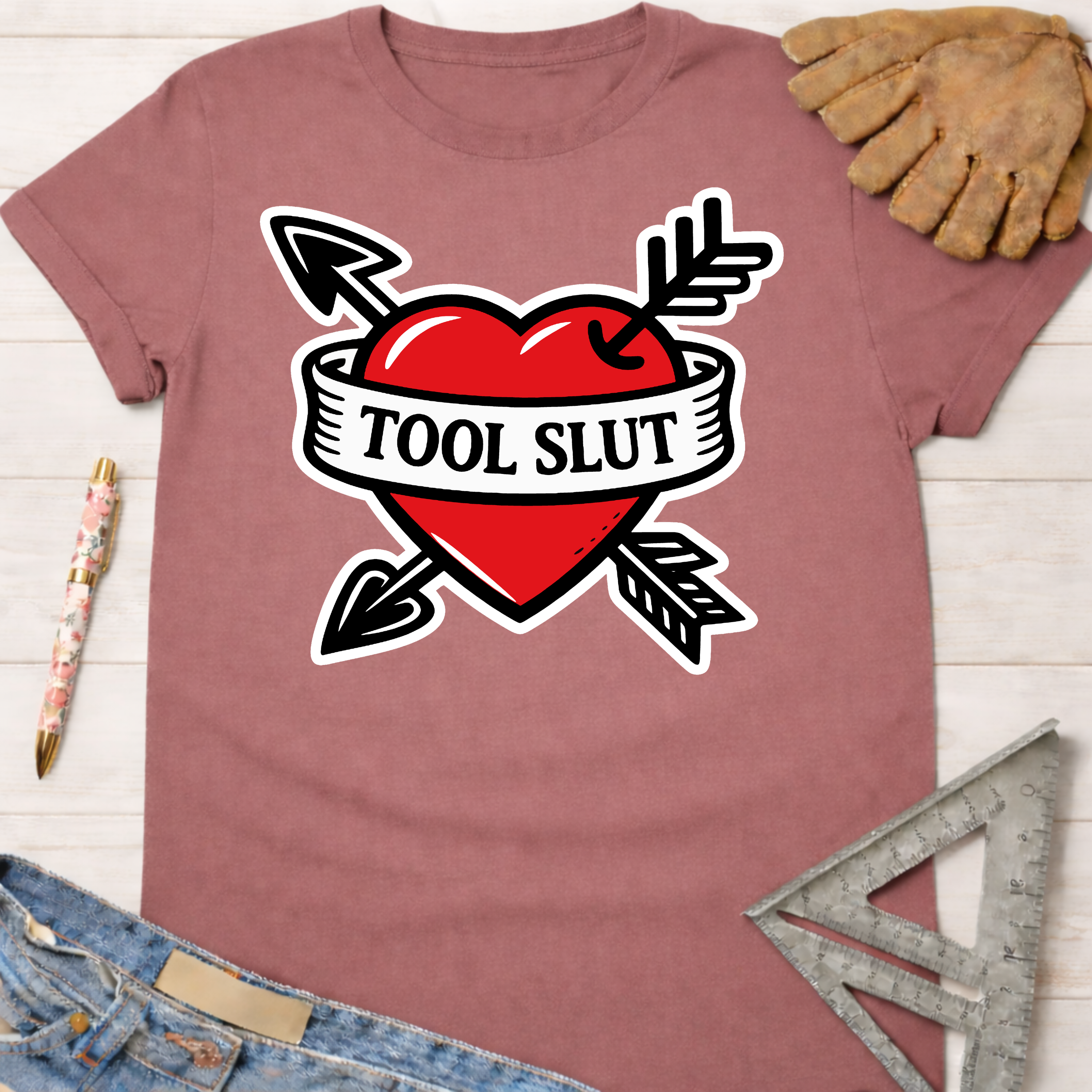 Women's funny woodworking graphic tee shirt for female woodworkers, makers, and DIY builders — Sawdust & Ponytails. Mauve t-shirt with a red heart, black arrows, and "TOOL SLUT" banner.