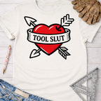 Women's funny woodworking graphic tee shirt for female woodworkers, makers, and DIY builders — Sawdust & Ponytails. White cotton tee with a red heart, crossed arrows, and "TOOL SLUT" banner.