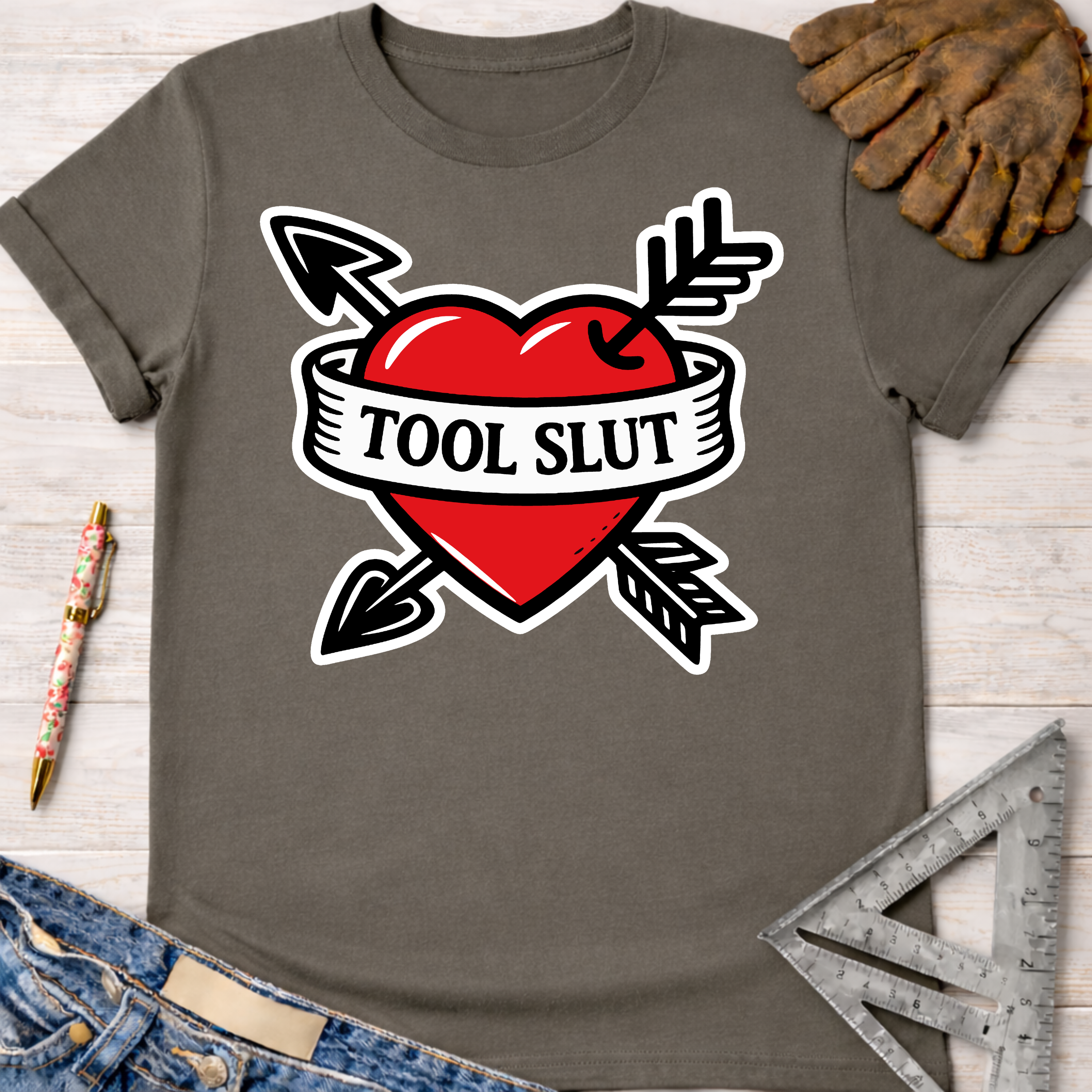 Women's funny woodworking graphic tee shirt for female woodworkers, makers, and DIY builders — Sawdust & Ponytails. Dark gray cotton tee with a red heart, crossed arrows, and "TOOL SLUT" banner.