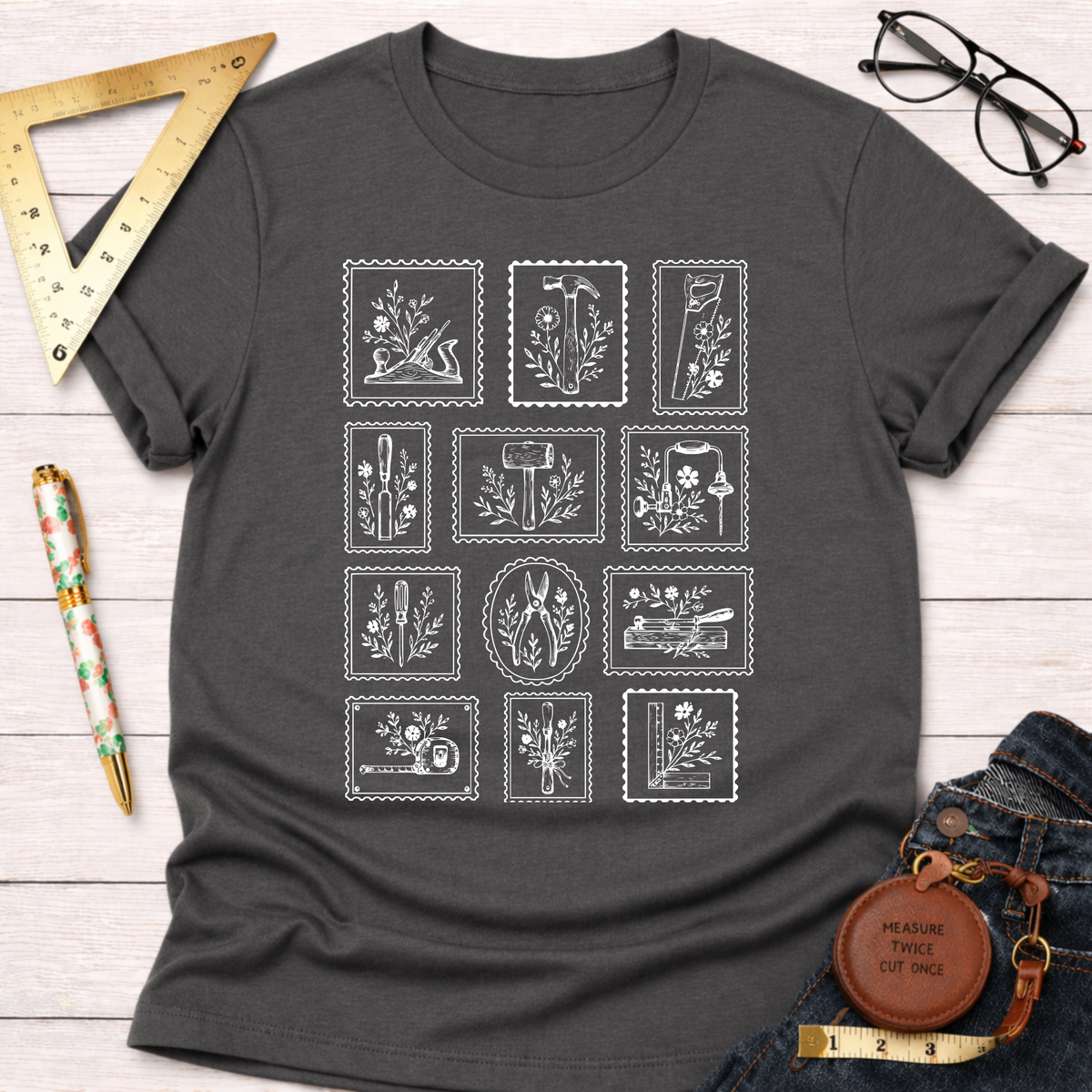 Charcoal gray Tool Stamps T-shirt with white floral woodworking tool graphics, styled with jeans and glasses.
