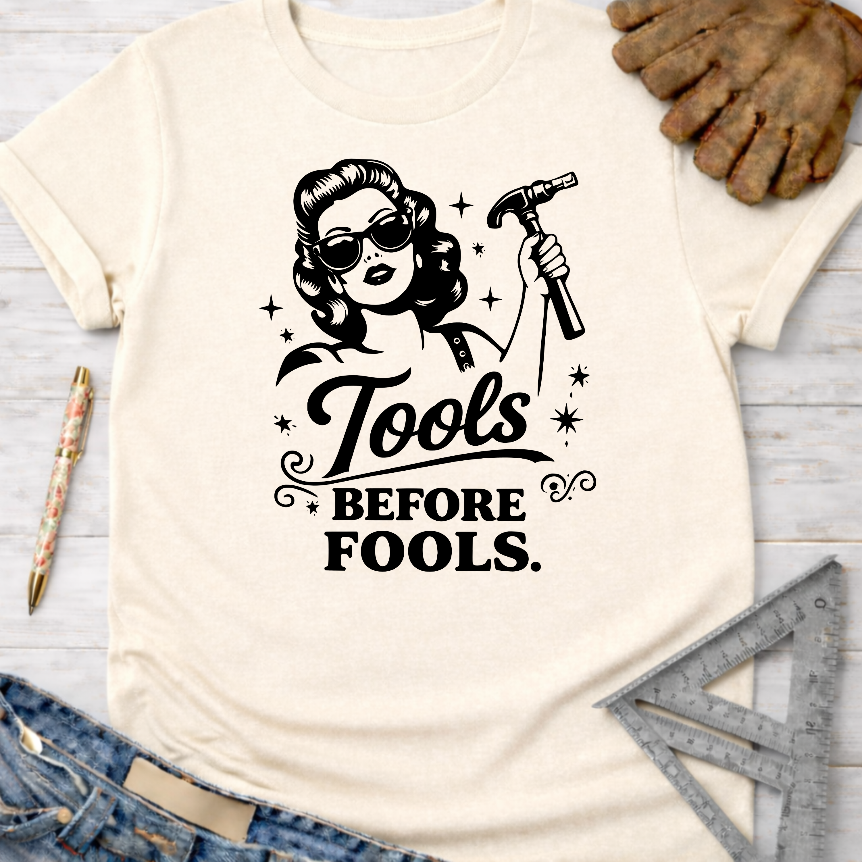 Women's funny woodworking graphic tee shirt for female woodworkers, makers, and DIY builders — Sawdust & Ponytails. Cream t-shirt with "Tools Before Fools" graphic featuring a retro woman holding a hammer.