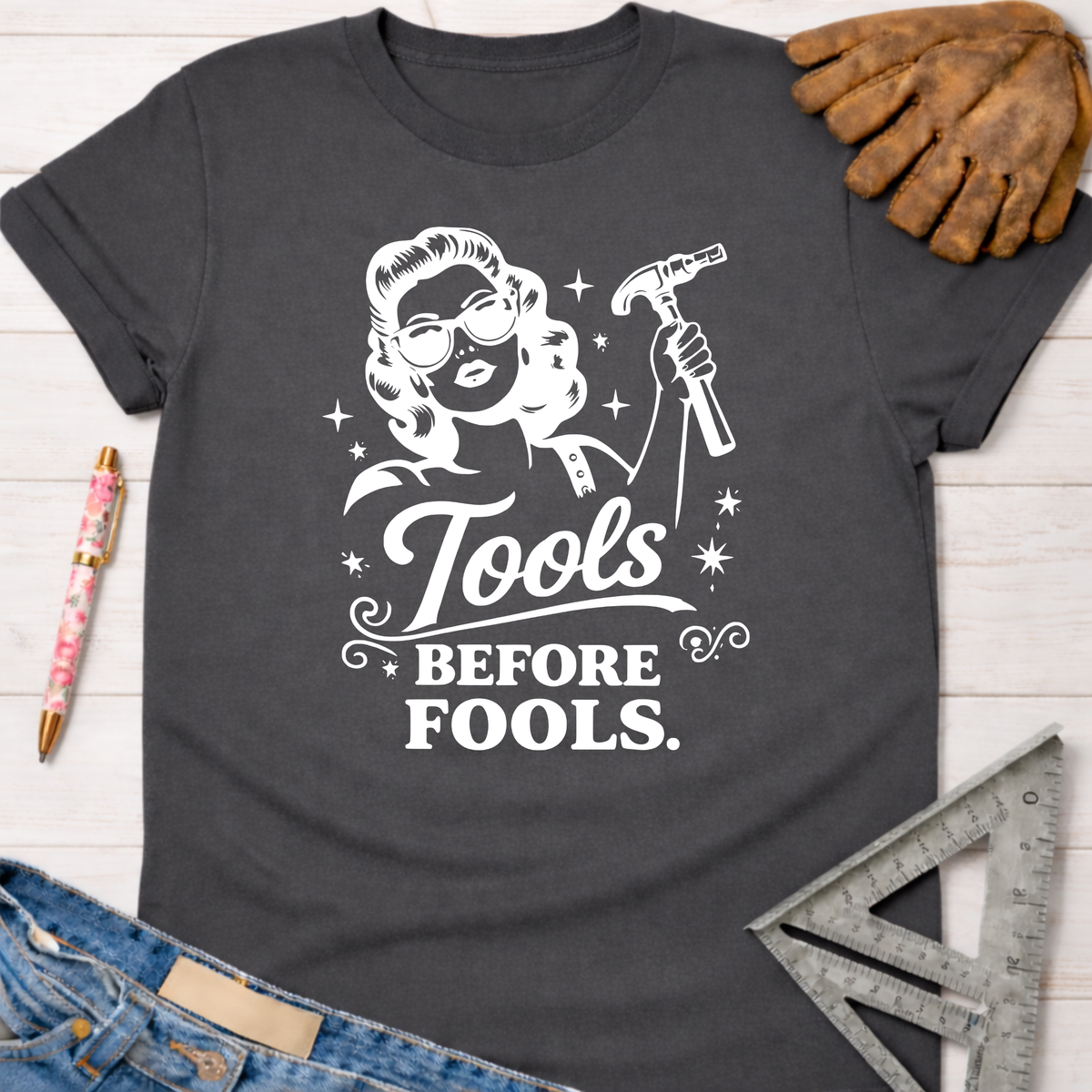 Women's funny woodworking graphic tee shirt for female woodworkers, makers, and DIY builders — Sawdust & Ponytails. Dark gray cotton tee with "Tools Before Fools" text and a retro woman holding a hammer.