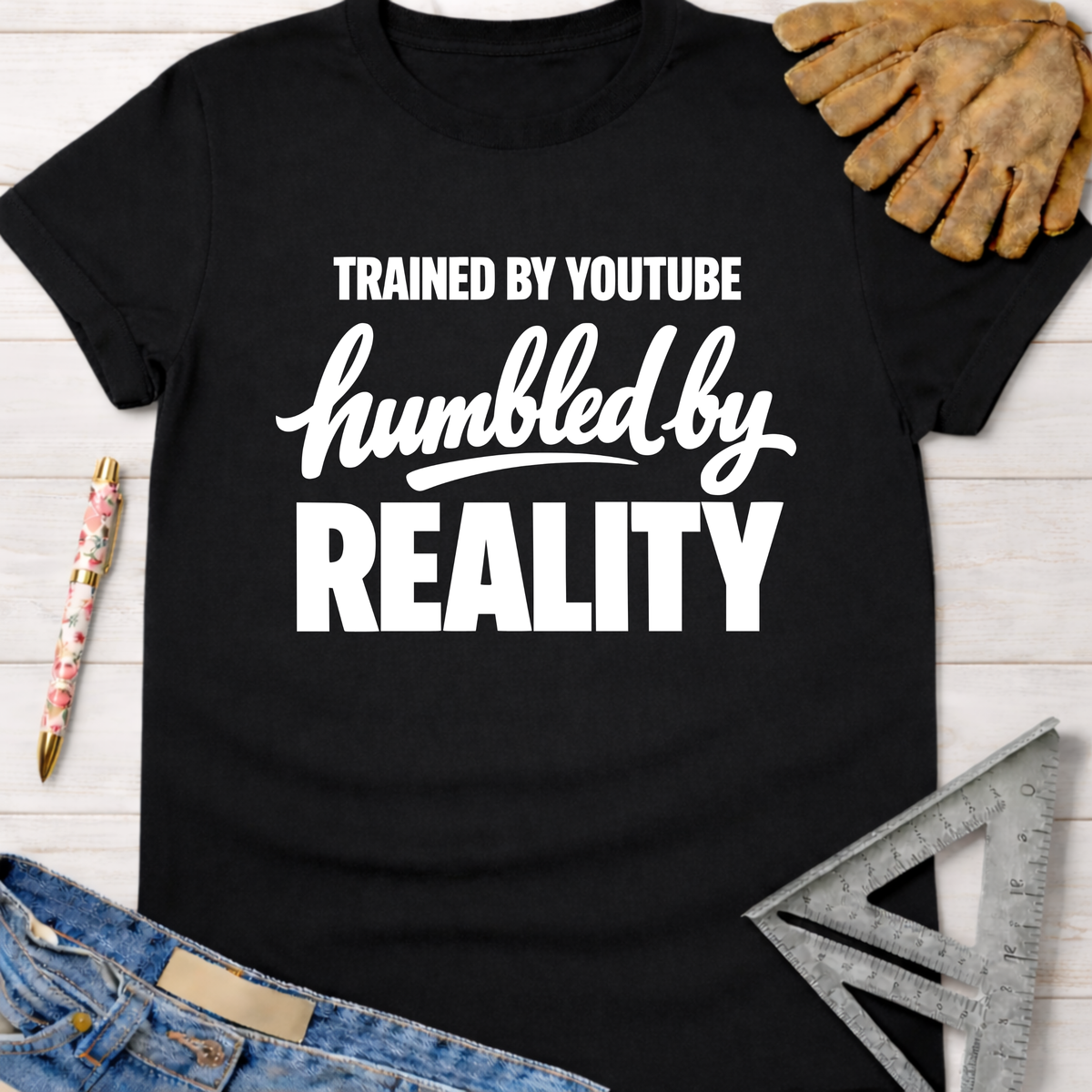 Black cotton t-shirt with "Trained By YouTube Humbled By REALITY" graphic. Women's funny woodworking graphic tee shirt for female woodworkers, makers, and DIY builders — Sawdust & Ponytails.