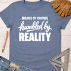 Women's funny woodworking graphic tee shirt for female woodworkers, makers, and DIY builders — Sawdust & Ponytails. Blue cotton t-shirt with "Trained By YouTube Humbled By Reality" in white text.