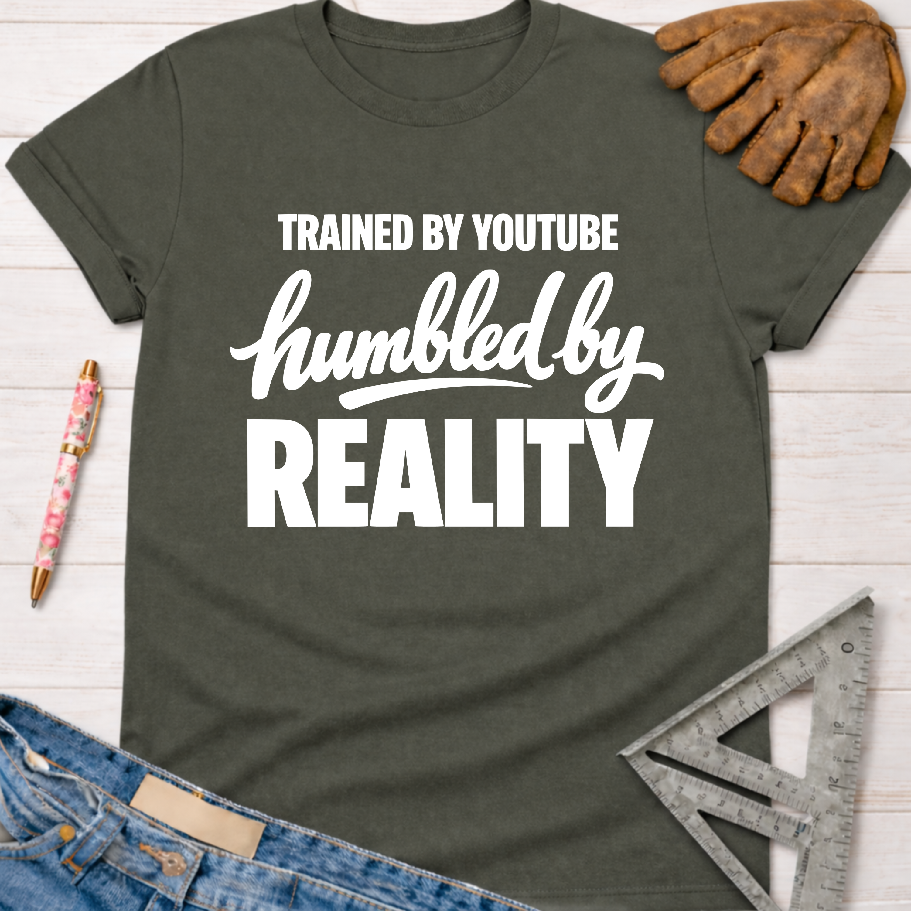 Women's funny woodworking graphic tee shirt for female woodworkers, makers, and DIY builders — Sawdust & Ponytails. Dark gray cotton tee with "Trained By YouTube Humbled By Reality" in white text.