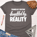 Women's funny woodworking graphic tee shirt for female woodworkers, makers, and DIY builders — Sawdust & Ponytails. Dark gray cotton t-shirt with "Trained By YouTube Humbled By Reality" in white text.