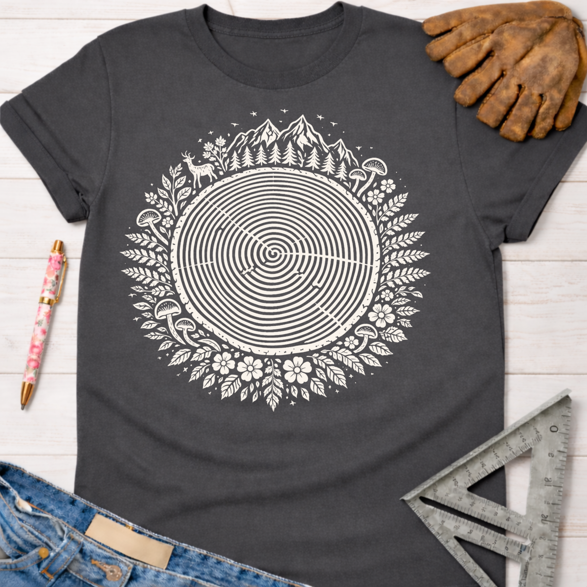 Women's funny woodworking graphic tee shirt for female woodworkers, makers, and DIY builders — Sawdust & Ponytails. Dark gray t-shirt with a white tree ring design surrounded by nature elements.