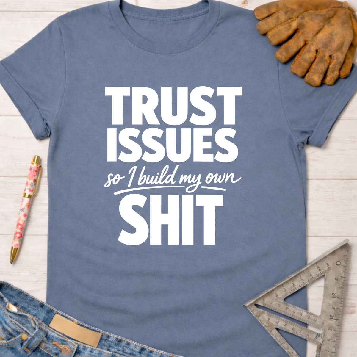 Women's funny woodworking graphic tee shirt for female woodworkers, makers, and DIY builders — Sawdust & Ponytails. Blue cotton t-shirt with "TRUST ISSUES so I build my own SHIT" in white text, surrounded by tools.