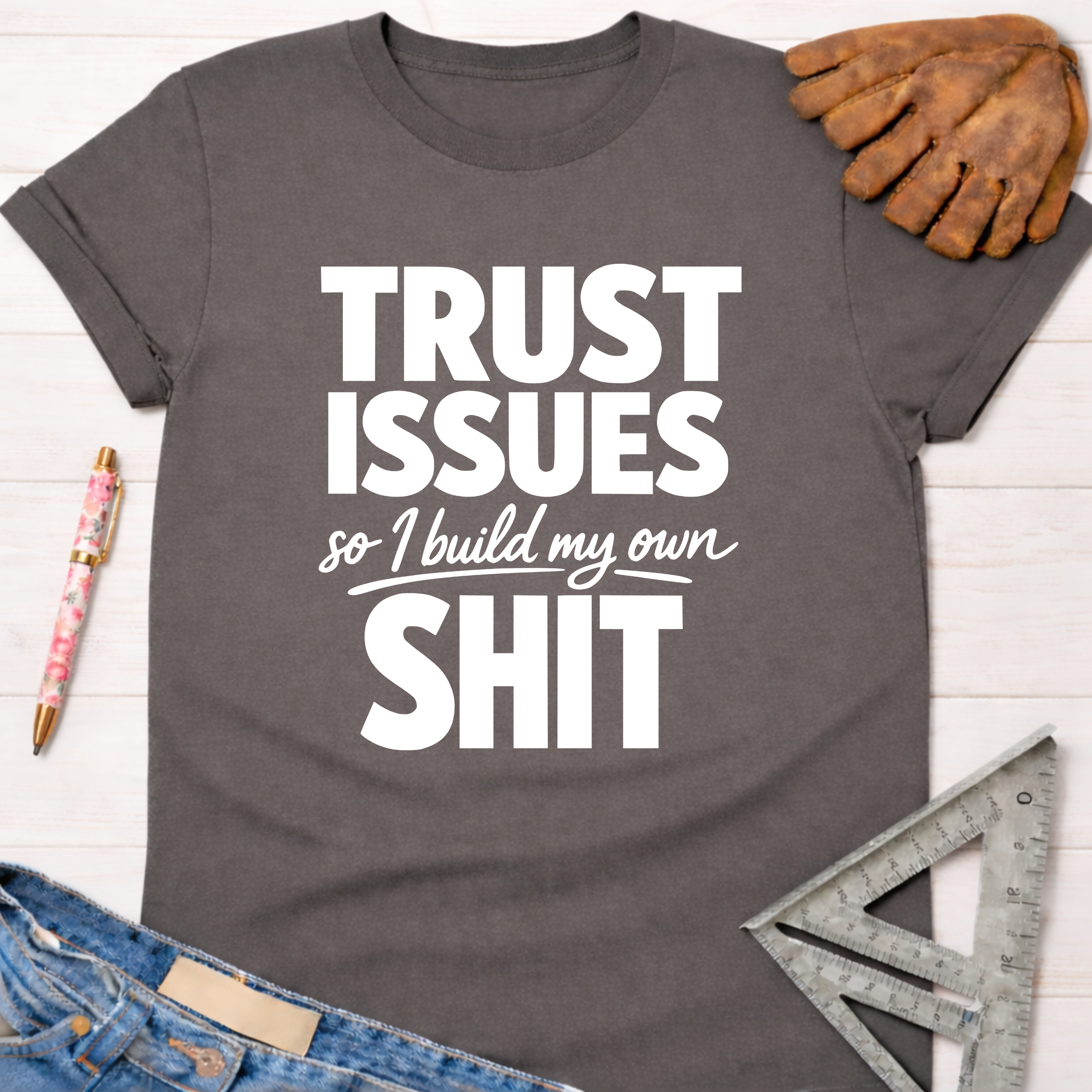 Women's funny woodworking graphic tee shirt for female woodworkers, makers, and DIY builders — Sawdust & Ponytails. Dark gray cotton tee with "TRUST ISSUES so I build my own SHIT" in white text.