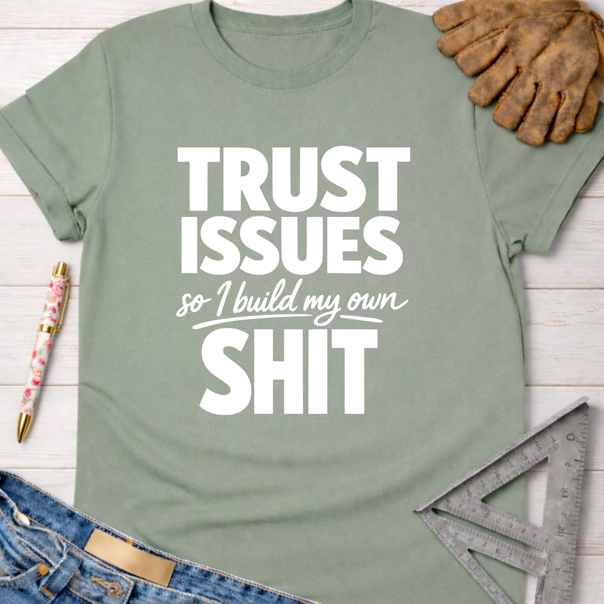 Women's funny woodworking graphic tee shirt for female woodworkers, makers, and DIY builders — Sawdust & Ponytails. Sage green cotton tee with "TRUST ISSUES so I build my own SHIT" in white text.