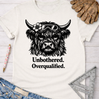 Women's funny woodworking graphic tee shirt for female woodworkers, makers, and DIY builders — Sawdust & Ponytails. Cream tee with black Highland cow wearing goggles and flower, "Unbothered. Overqualified." text.
