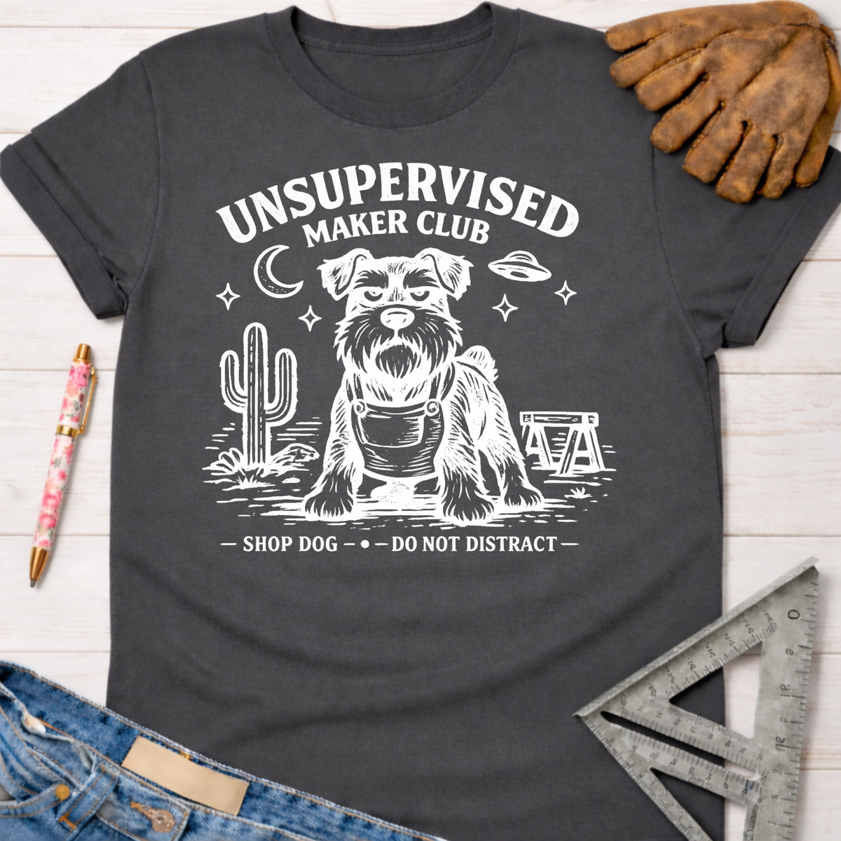 Women's funny woodworking graphic tee shirt for female woodworkers, makers, and DIY builders — Sawdust & Ponytails. Dark gray cotton tee with a white graphic of a dog in overalls, "Unsupervised Maker Club," and "Shop Dog - Do Not Distract.