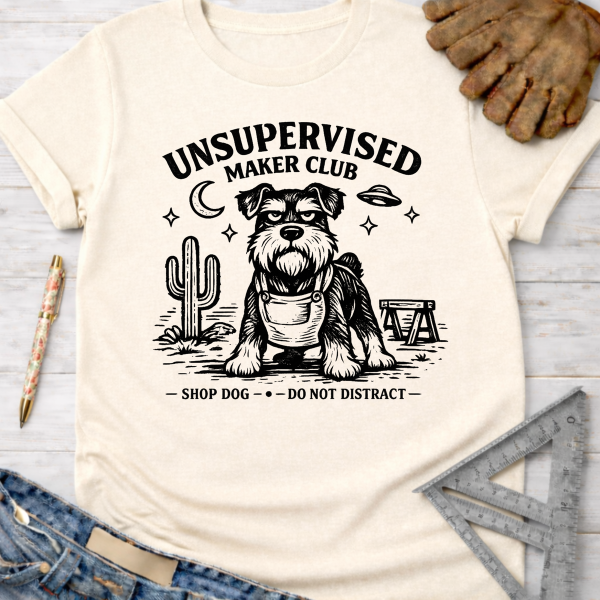 Women's funny woodworking graphic tee shirt for female woodworkers, makers, and DIY builders — Sawdust & Ponytails. Cream t-shirt with "Unsupervised Maker Club" and a schnauzer in overalls.