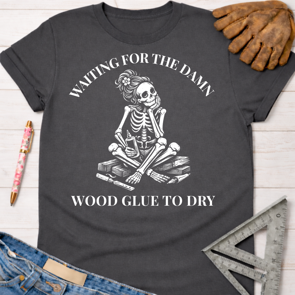 Women's funny woodworking graphic tee shirt for female woodworkers, makers, and DIY builders — Sawdust & Ponytails. Dark gray t-shirt with a white graphic of a female skeleton impatiently waiting for wood glue to dry.