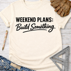 Cream "Weekend Plans: Build Something" graphic tee with work gloves, jeans, pen, and ruler.