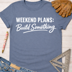 Women's funny woodworking graphic tee shirt for female woodworkers, makers, and DIY builders — Sawdust & Ponytails. Blue cotton t-shirt with "Weekend Plans: Build Something" in white text, beside work gloves, jeans, and a ruler.