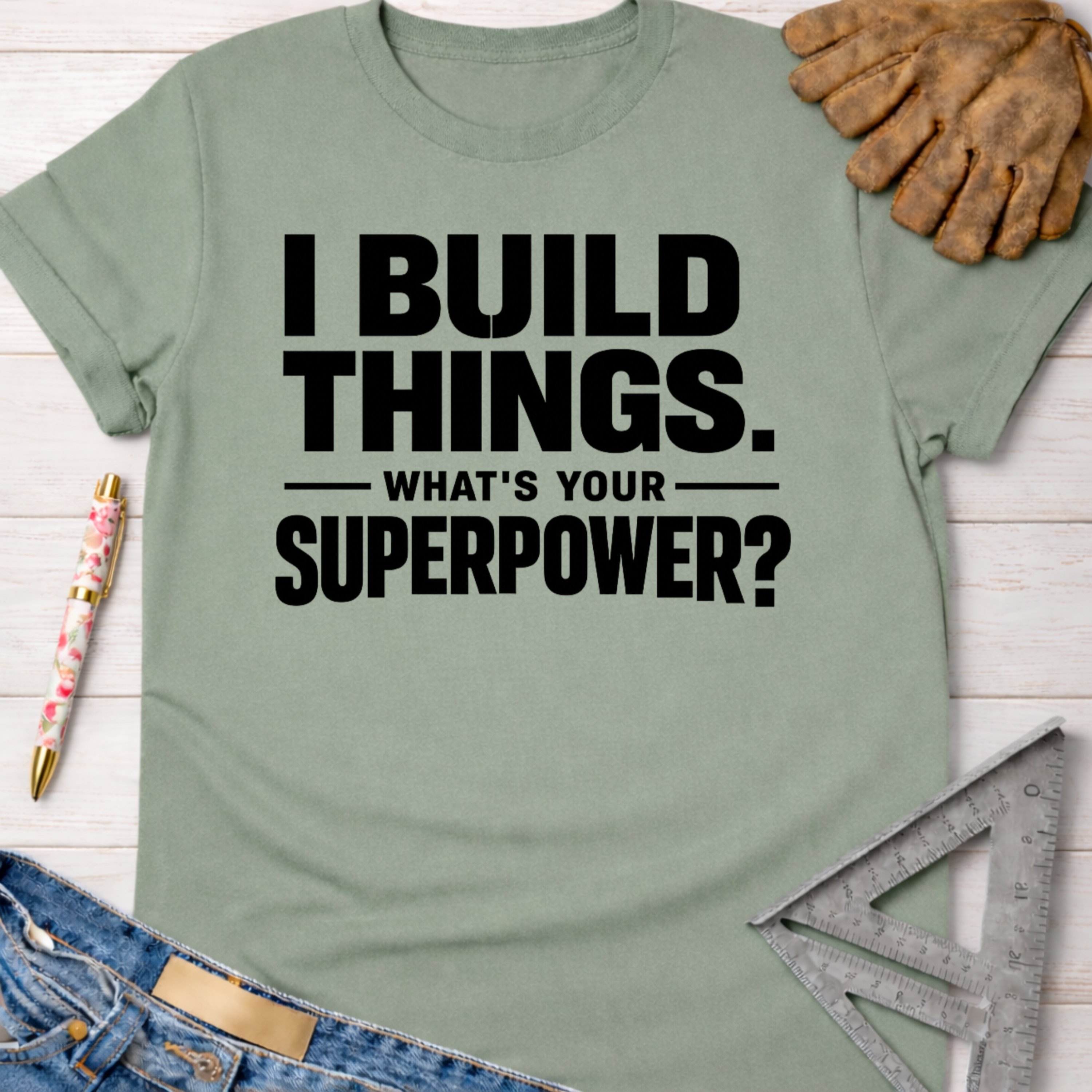Women's funny woodworking graphic tee shirt for female woodworkers, makers, and DIY builders — Sawdust & Ponytails. Sage green cotton tee with "I BUILD THINGS. WHAT'S YOUR SUPERPOWER?" in black text.