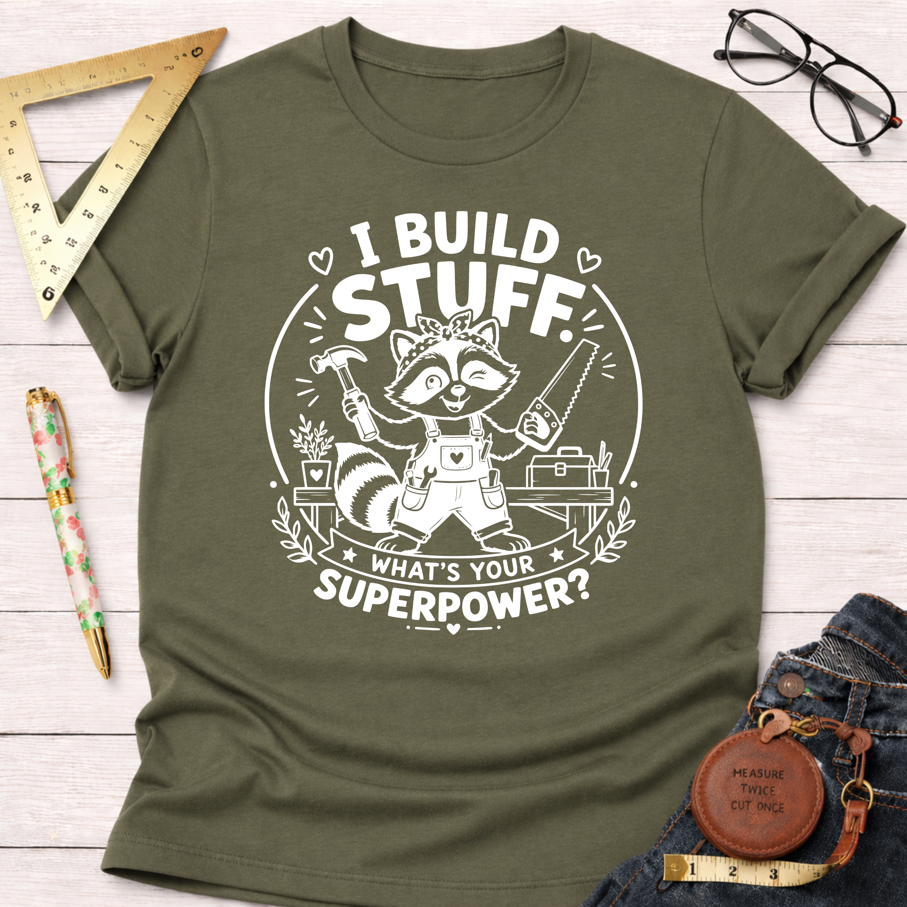 Olive green cotton t-shirt with a white graphic of a raccoon builder holding a hammer and saw.