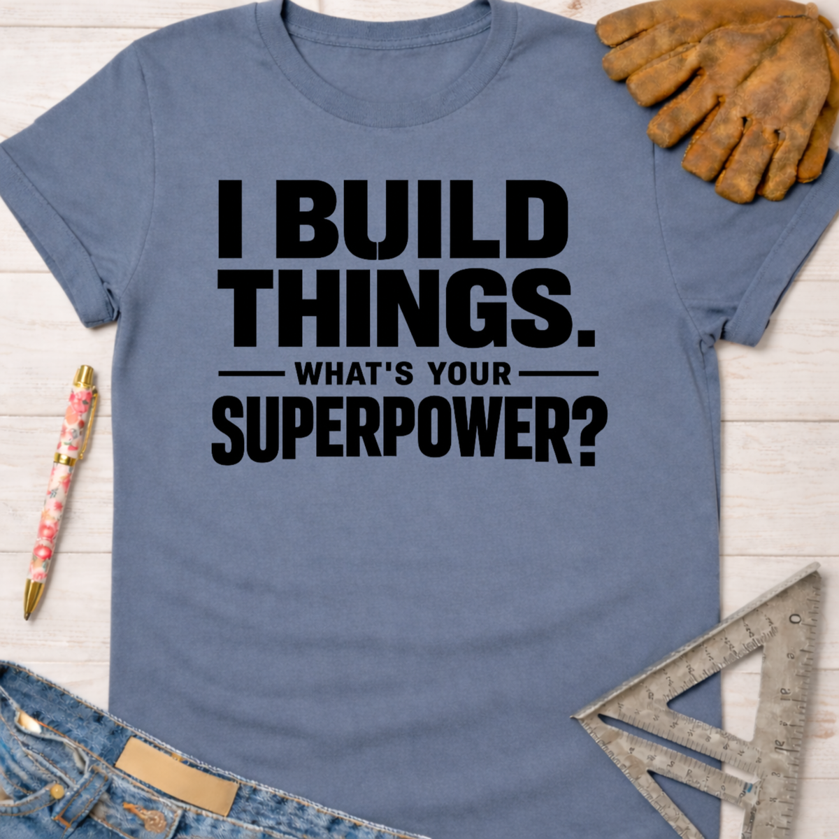 Women's funny woodworking graphic tee shirt for female woodworkers, makers, and DIY builders — Sawdust & Ponytails. Blue cotton t-shirt with "I BUILD THINGS. WHAT'S YOUR SUPERPOWER?" in black text.