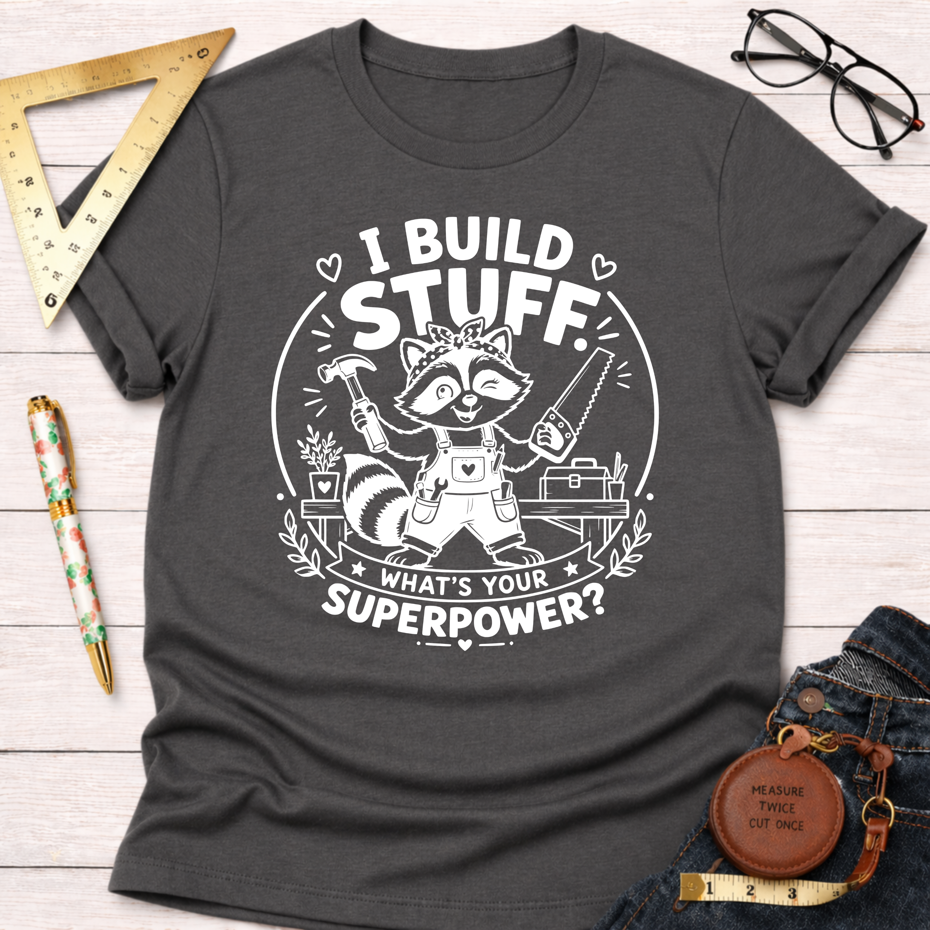 Charcoal gray cotton t-shirt with a white graphic of a raccoon builder holding tools and "I Build Stuff. What's Your Superpower?" text.