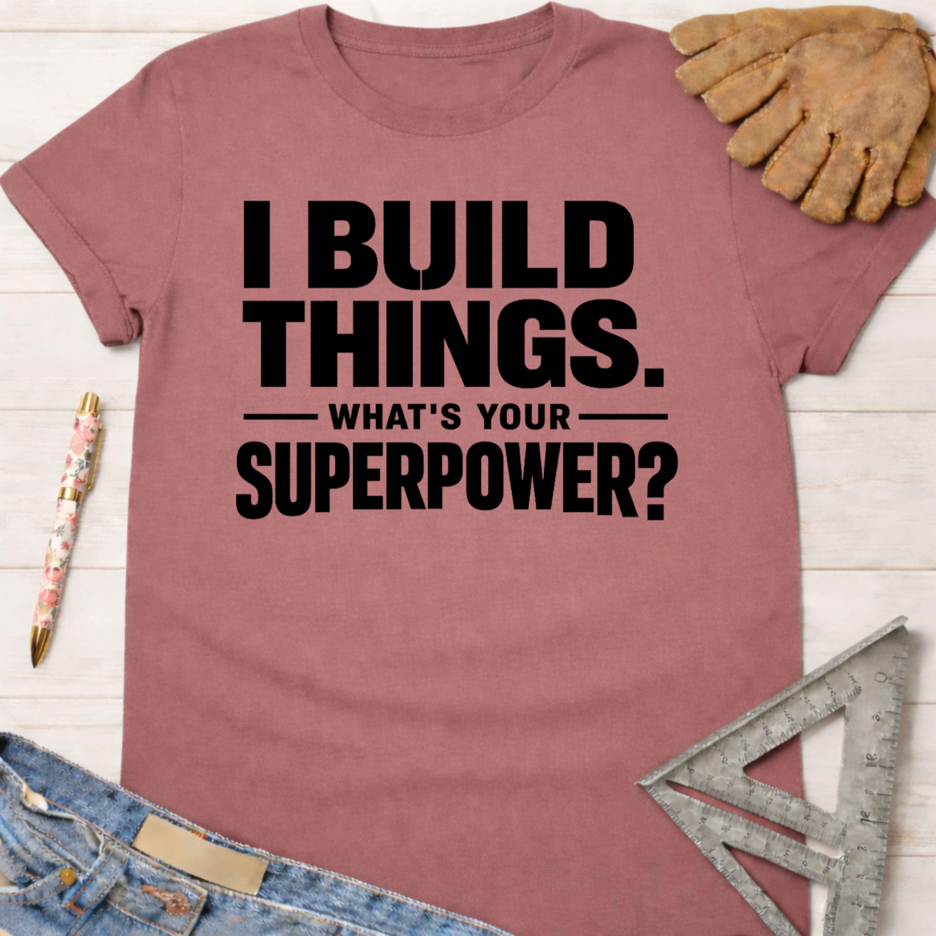 Women's funny woodworking graphic tee shirt for female woodworkers, makers, and DIY builders — Sawdust & Ponytails. Mauve t-shirt with "I BUILD THINGS. WHAT'S YOUR SUPERPOWER?" in black text.