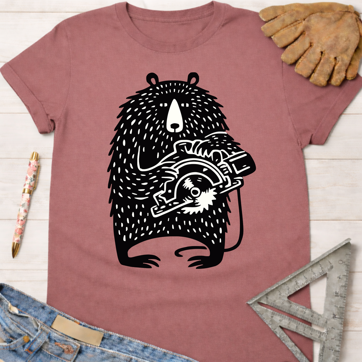 Women's funny woodworking graphic tee shirt for female woodworkers, makers, and DIY builders — Sawdust & Ponytails. Mauve t-shirt with a black bear holding a circular saw graphic.