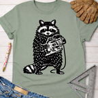 Women's funny woodworking graphic tee shirt for female woodworkers, makers, and DIY builders — Sawdust & Ponytails. Sage green tee with a black and white raccoon holding a jigsaw.