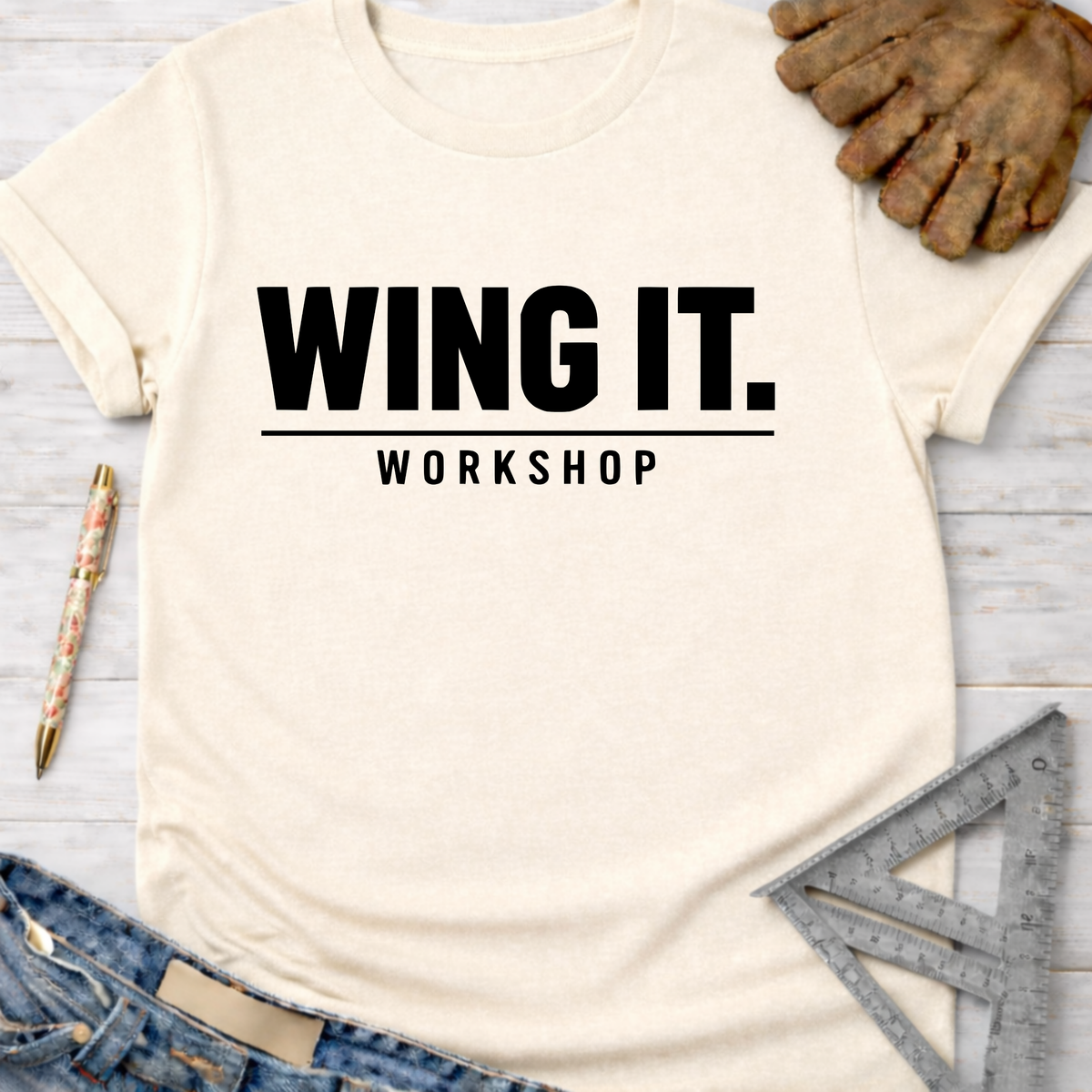 Women's funny woodworking graphic tee shirt for female woodworkers, makers, and DIY builders — Sawdust & Ponytails. Cream t-shirt with "WING IT. WORKSHOP" in black text, styled with jeans, work gloves, and tools.