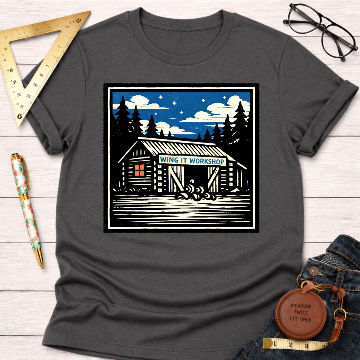 Charcoal gray "Wing It Workshop" graphic tee with a rustic cabin design under a starry sky.