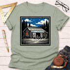 Sage green Wing It Workshop t-shirt with a graphic of a cabin workshop under a starry night sky.