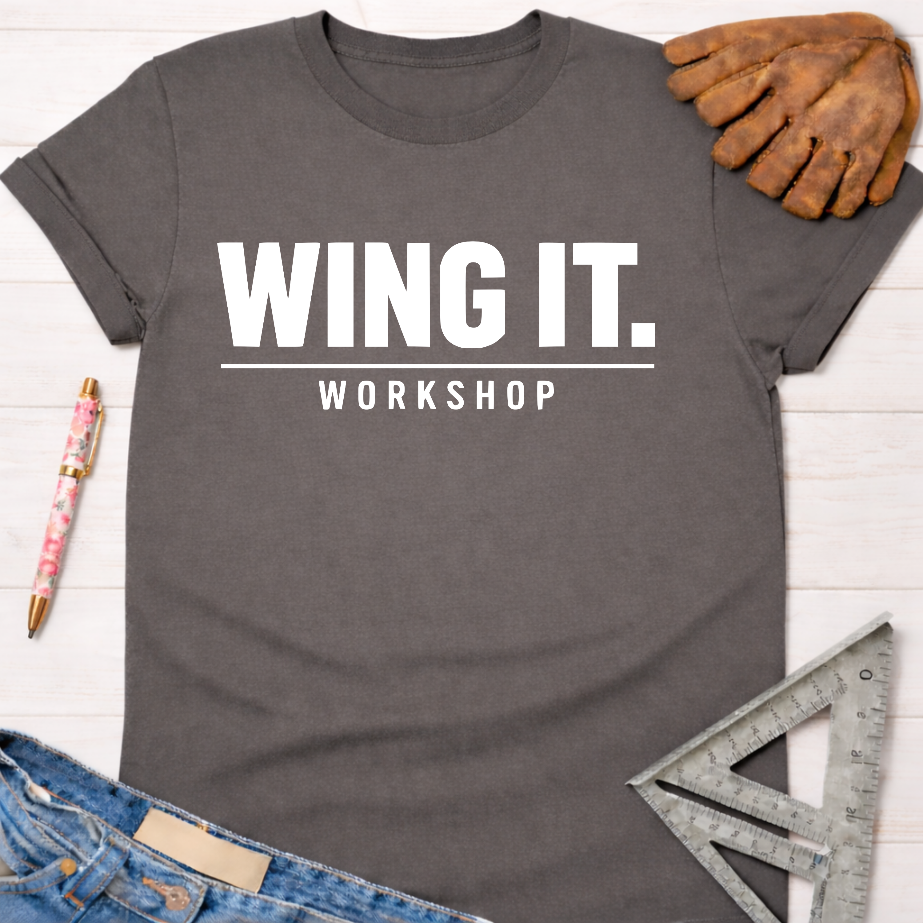 Women's funny woodworking graphic tee shirt for female woodworkers, makers, and DIY builders — Sawdust & Ponytails. Dark gray cotton "Wing It. Workshop" tee with jeans, work glove, pen, and speed square.
