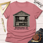 Pink t-shirt with "Winging It Workshop" shed graphic and "One Bad Cut At A Time" text.