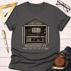 Charcoal gray t-shirt with a "Winging It Workshop" design featuring a detailed woodworking shed.