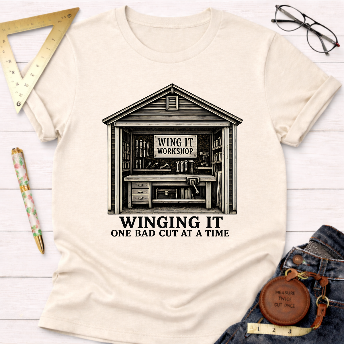 Cream t-shirt with "Winging It Workshop" shed design and "Winging It One Bad Cut At A Time" text.