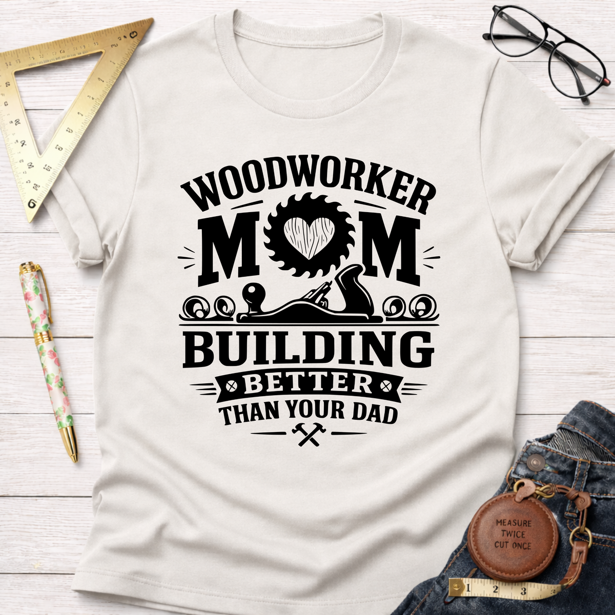 Women's funny woodworking graphic tee shirt for female woodworkers, makers, and DIY builders — Sawdust & Ponytails. Cream t-shirt with "Woodworker Mom Building Better Than Your Dad" graphic.